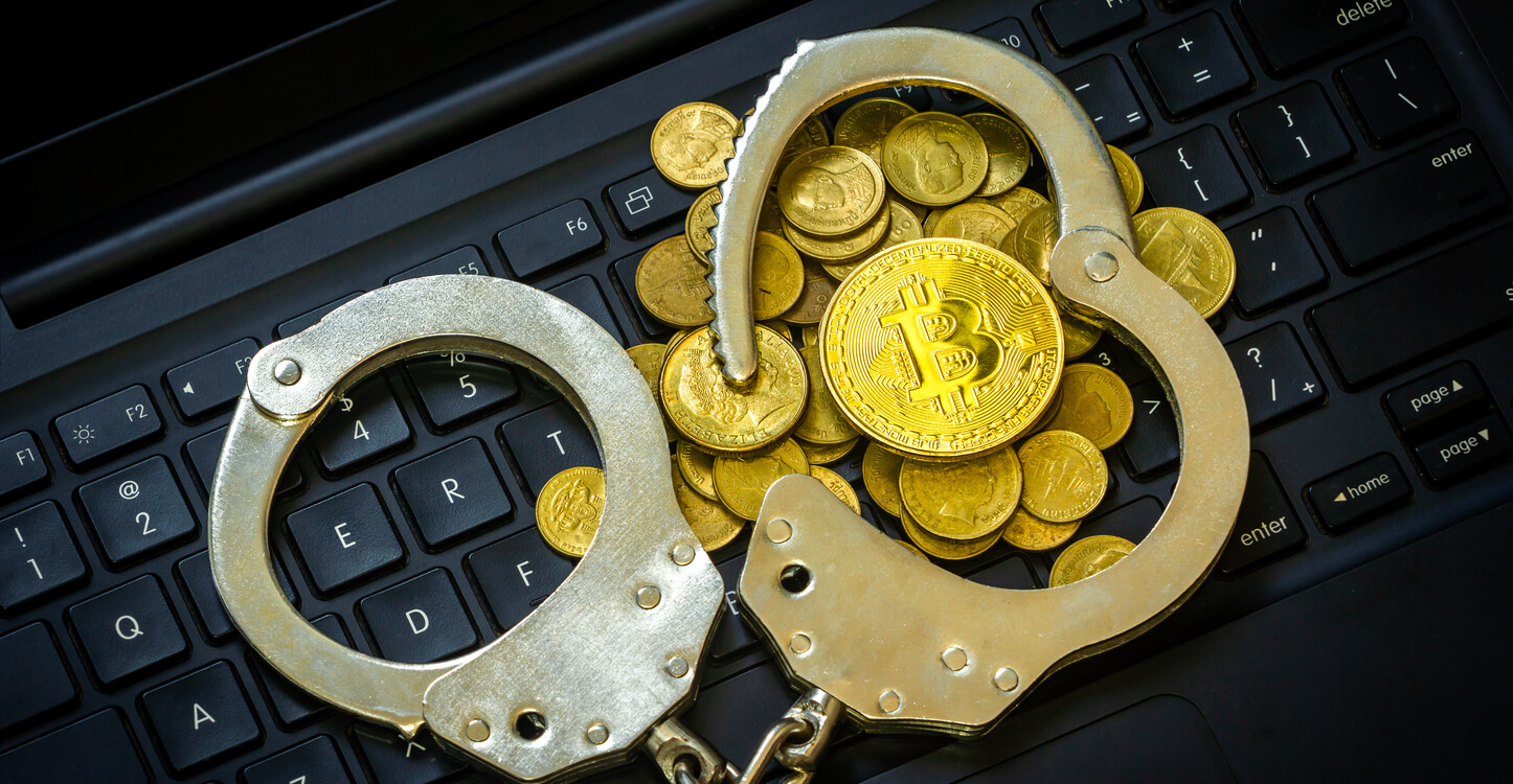 An image of golden Bitcoin with handcuffs on a computer keyboard