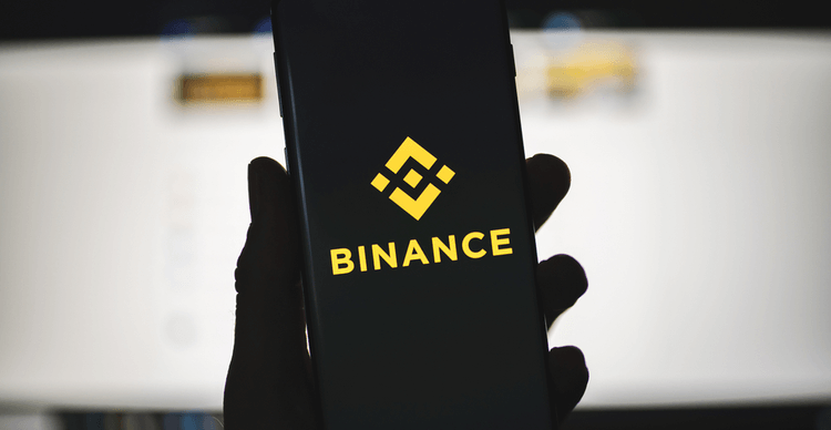 An image of a hand holding a phone displaying the Binance logo