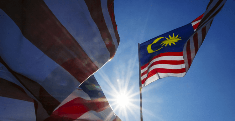 A Malaysian flag blowing in the wind with a bright sun shining from behind