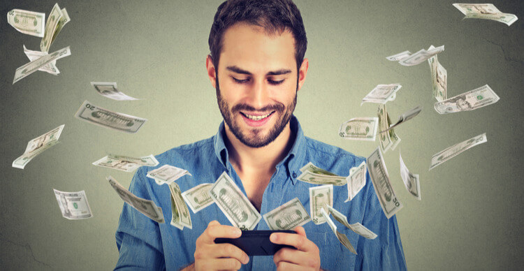 A man plays a game on his mobile phone, with paper money emanating from the device
