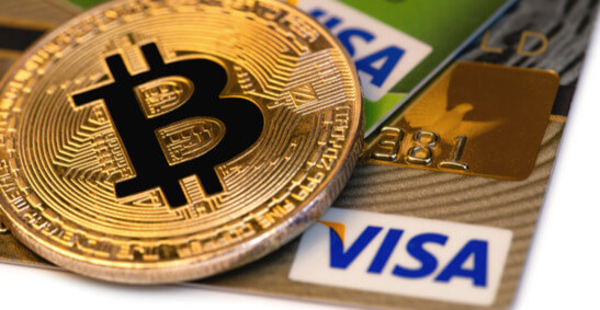 An image of a bitcoin resting on Visa cards