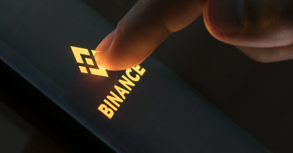 Foto van een vinger die op het Binance logo drukt