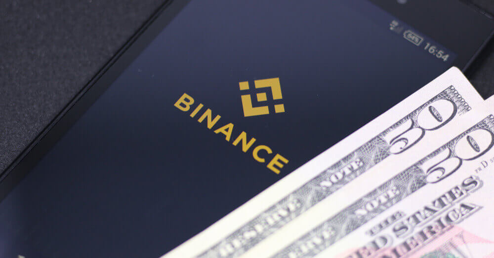 Een foto van het Binance logo op een smartphone, plus wat extra bankbiljetten