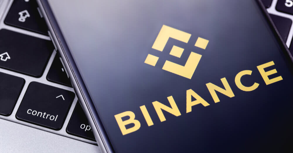 Un smartphone avec le logo de Binance à l'écran posé sur un ordinateur