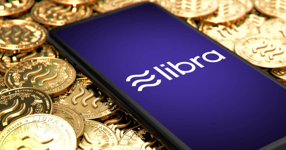 Un smartphone avec le logo de Libra à l'écran posé sur des pièces de Libra