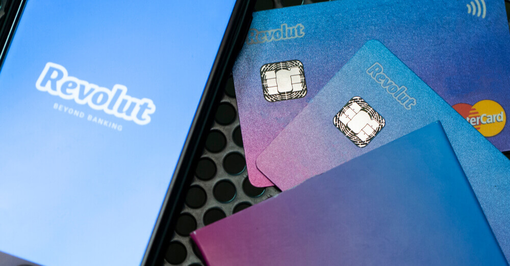 Un smartphone avec le logo de Revolut à l'écran et des cartes bancaires Revolut