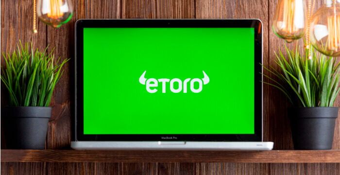 Un ordinateur avec le logo d’eToro à l’écran entouré de plantes