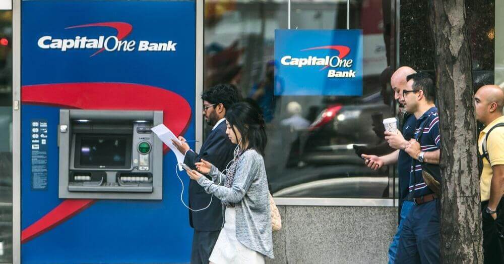 Image d'un distributeur automatique de billets Capital One avec des gens marchant devant ce dernier