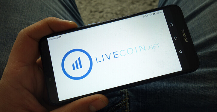 Homme tenant un smartphone avec le logo Livecoin de l'exchange de crypto-monnaies