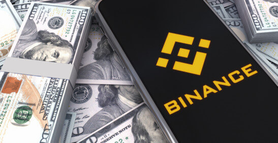 Un téléphone portable avec le logo de Binance sur fond de billets de 100 dollars.