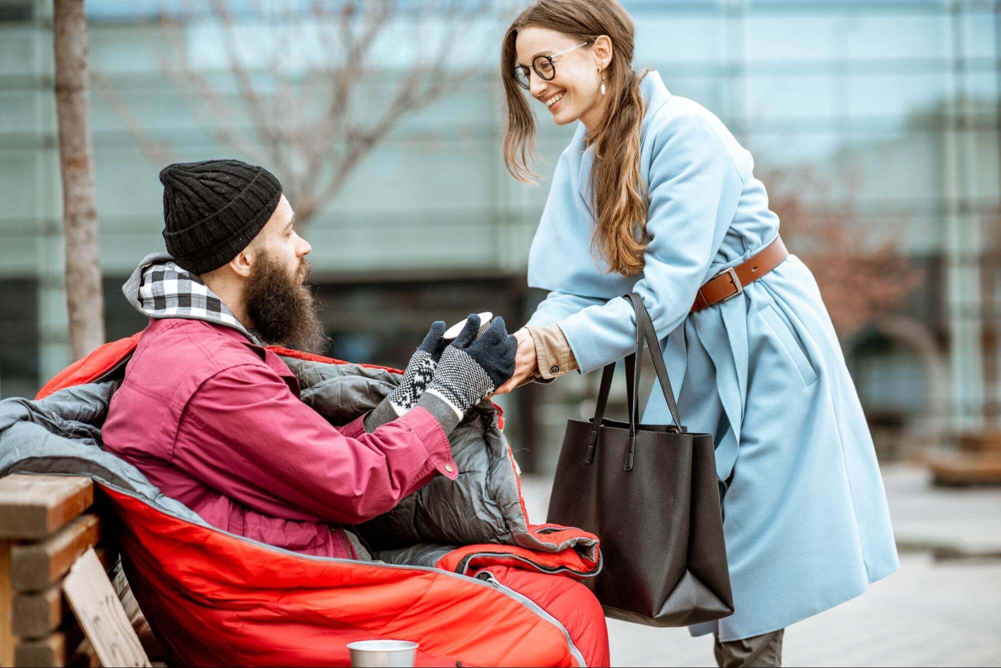 Une femme donne de l'argent à un homme démuni assis sur un banc