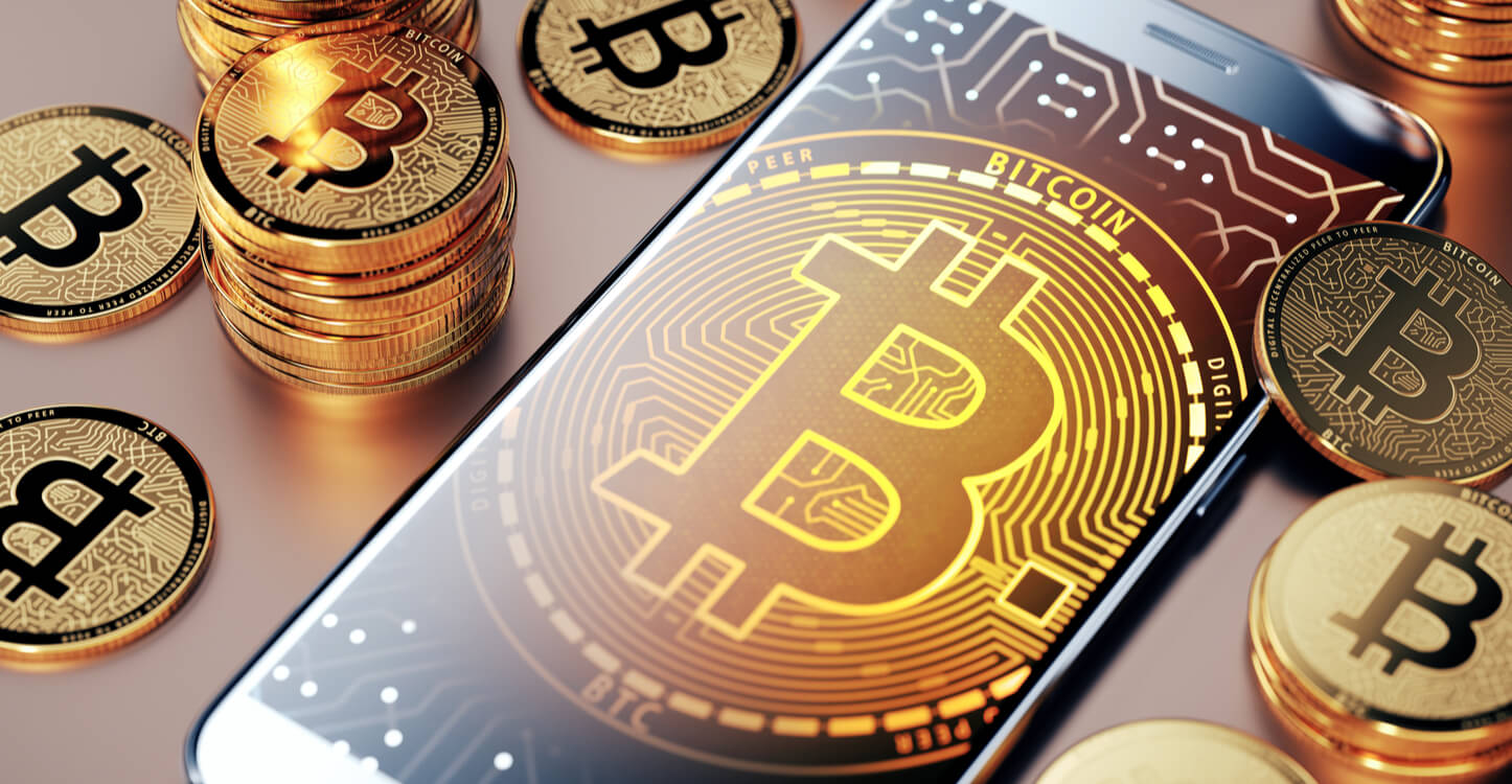 A phone with BTC symbol surrounded by physical bitcoins